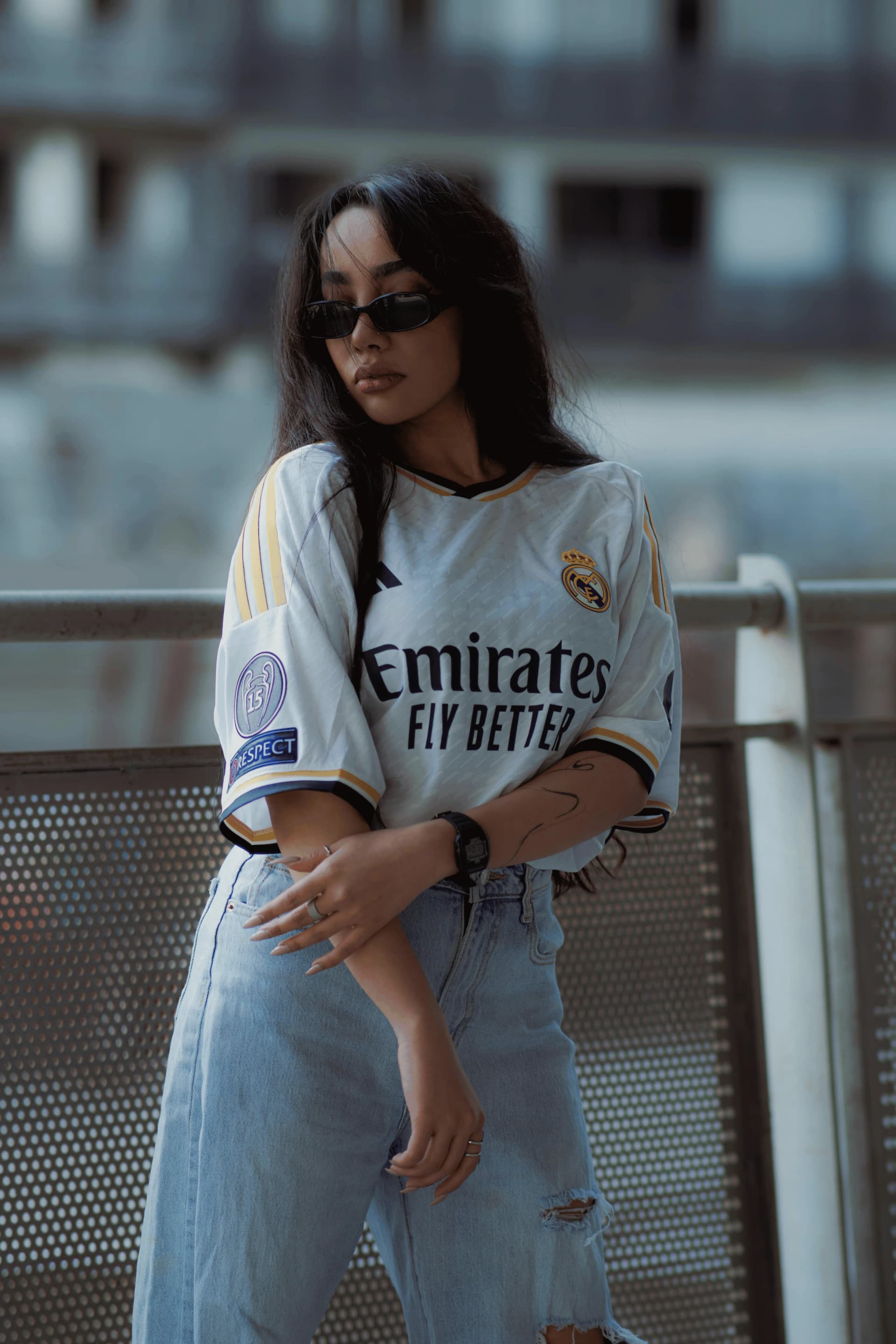 Person trägt ein weißes Vintage Real Madrid Trikot mit Jeans und Sonnenbrille im urbanen Streetwear Look.